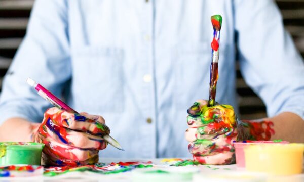 person at table with paintbrush and paint on hands