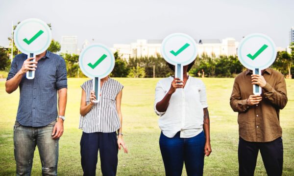 four people holding up checkmark signs in park