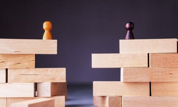 Two sets of Jenga blocks with a gap between them. A yellow game piece sits atop one stack and a black game piece atop the other.