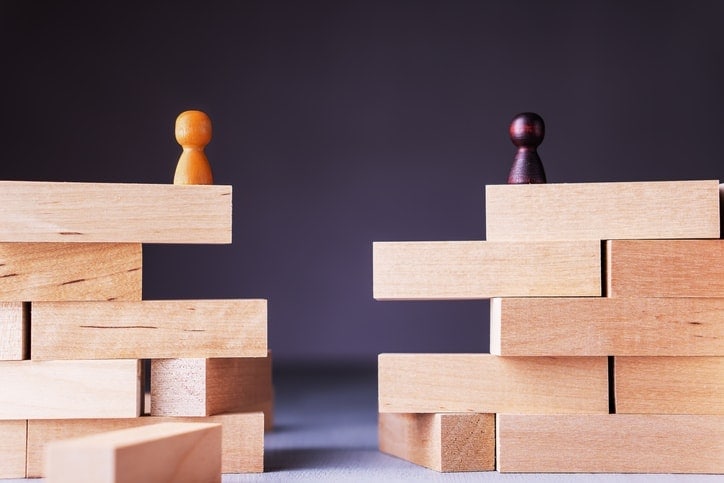 Two sets of Jenga blocks with a gap between them. A yellow game piece sits atop one stack and a black game piece atop the other.