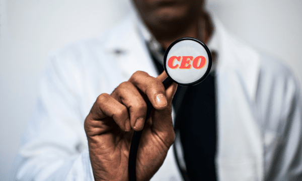 A doctor holding a stethoscope face-up (hand and stethoscope far in the foreground). The face of the stethoscope says "CEO" on it in coral lettering.