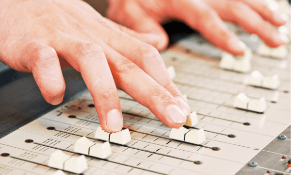 Two hands adjusting white sliding buttons on a sound mixing board