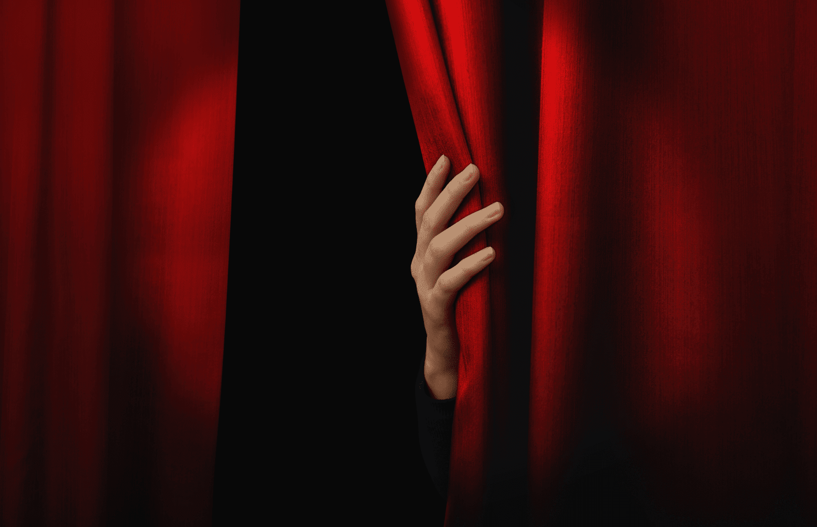 Close-up of a woman's hand opening a red theater curtain