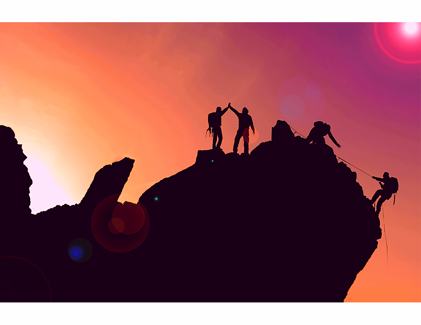Three hikers in silhouette helping pull a fourth hiker up the side of a mountain, with a orange and pink sunset in the background.